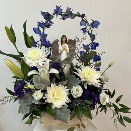 White and blue floral arrangement with an angel figurine in a wooden box