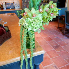 Tall green floral arrangement with orchids and hanging amaranthus in a glass vase