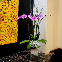 Purple orchids in a tall mirrored vase with green leaves