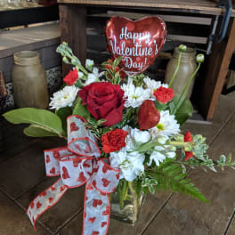 Red and white flower arrangement in a glass vase with a heart balloon