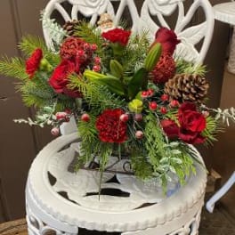 Red floral arrangement with pinecones in a white decorative chair