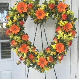 Heart-shaped floral wreath with orange gerberas and roses on an easel