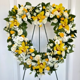 Heart-shaped floral wreath with yellow orchids and white roses on a stand