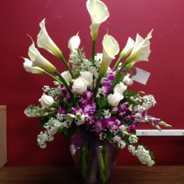 Tall bouquet of white calla lilies, white roses, and purple orchids in a glass vase