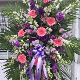 Standing floral spray with pink gerberas, purple blooms, and a lavender ribbon