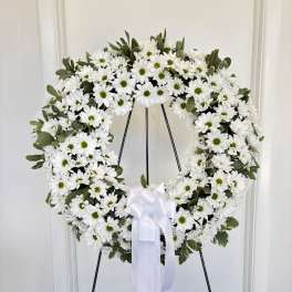 White daisy wreath on a stand with a white ribbon