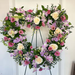 Heart-shaped floral wreath with pink, lavender, and cream blooms on a stand