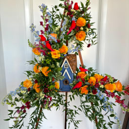 Tall floral easel arrangement with orange roses, blue flowers, and red cardinals