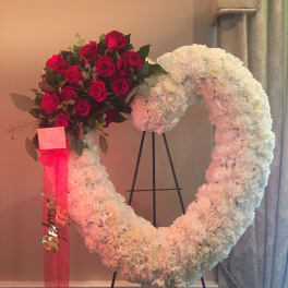 Heart-shaped white floral wreath with red roses and a pink ribbon