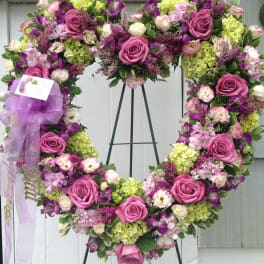 Heart-shaped floral wreath with pink roses and purple blooms on an easel