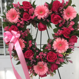 Heart-shaped wreath of pink roses and gerbera daisies with a pink ribbon
