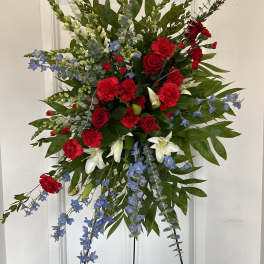 Standing floral spray with red roses, red carnations, white lilies, and blue flowers