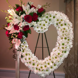 Heart-shaped floral wreath with red roses and white daisies on a stand
