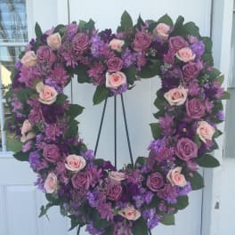 Heart-shaped floral wreath with pink and purple roses on a stand