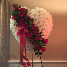 Heart-shaped floral tribute with red roses and white flowers on a stand