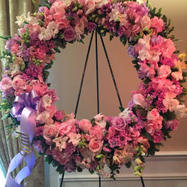 Pink and purple floral wreath on a black stand with a lavender ribbon