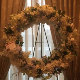 Large white floral wreath on a black stand with a ribbon bow