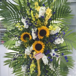 Large standing floral spray with sunflowers, white blooms, and palm fronds