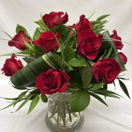 Arrangement of red roses with looped green leaves in a clear glass vase