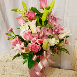Pink and white floral arrangement in a pink vase with a ribbon bow