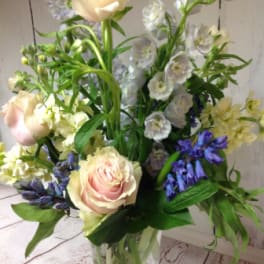Tall mixed bouquet of pale pink roses and soft blue flowers in a clear glass vase