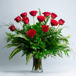Red roses arranged in a clear glass vase with lush greenery