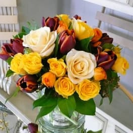 Round bouquet of white and yellow roses with burgundy tulips in a clear glass vase