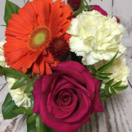 Compact arrangement with orange gerbera, pink rose, white carnations, and red accent blooms.