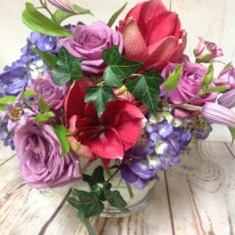Low glass vase of purple roses, blue hydrangeas, and red amaryllis blooms in a compact arrangement
