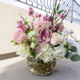 Low round arrangement of pink roses, orchids, and white hydrangeas in a clear glass bowl vase