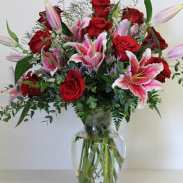 Tall arrangement of red roses and pink lilies in a clear glass vase