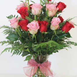 Tall arrangement of red and pink roses in a clear glass vase with a pink bow