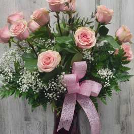 Pink roses arranged in a dark glass vase with a pink ribbon