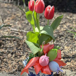 Potted red tulips in a blue and white ceramic container with ribbon and pastel egg accents