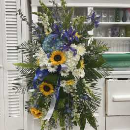 Tall standing floral spray with sunflowers, white daisies, and blue flowers