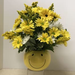 Yellow and white daisy bouquet in a smiley-face vase