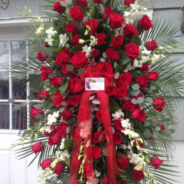 Tall standing spray of red roses with white orchids and a red ribbon