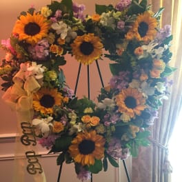 Heart-shaped floral wreath with sunflowers and pastel blooms on an easel