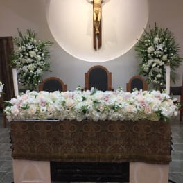 White floral altar arrangement beneath a crucifix in a church