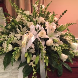 Large white funeral spray with lilies, roses, and ribbon