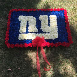 Rectangular floral tribute with white lettering, red border, and a red ribbon bow