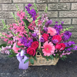 Basket arrangement of pink and purple flowers with roses and gerbera daisies