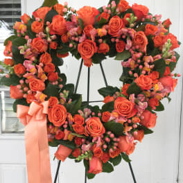 Heart-shaped wreath of orange roses with a peach ribbon on a stand