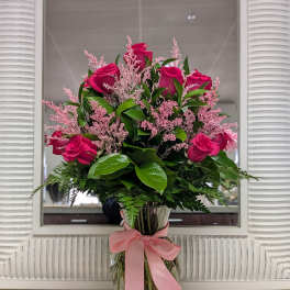 Tall arrangement of hot pink roses with pink filler in a clear glass vase tied with a pink bow.