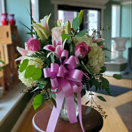 Bouquet of pink lilies, roses, and hydrangeas in a glass vase with a pink ribbon
