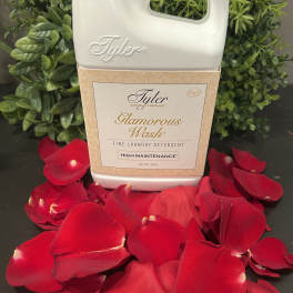 Laundry detergent bottle surrounded by red rose petals and greenery