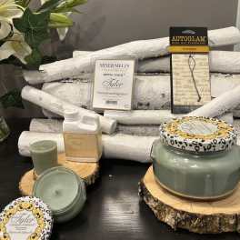 Assorted candles and fragrance products arranged on wood slices with white branches.