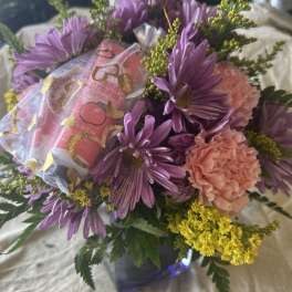 Purple daisies and peach carnations in a small vase with a gift bag