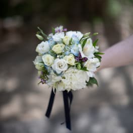 Handheld bouquet of white and pale blue flowers with dark ribbon tails