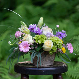 Mixed bouquet in a rustic container with pink, purple, white, and green blooms